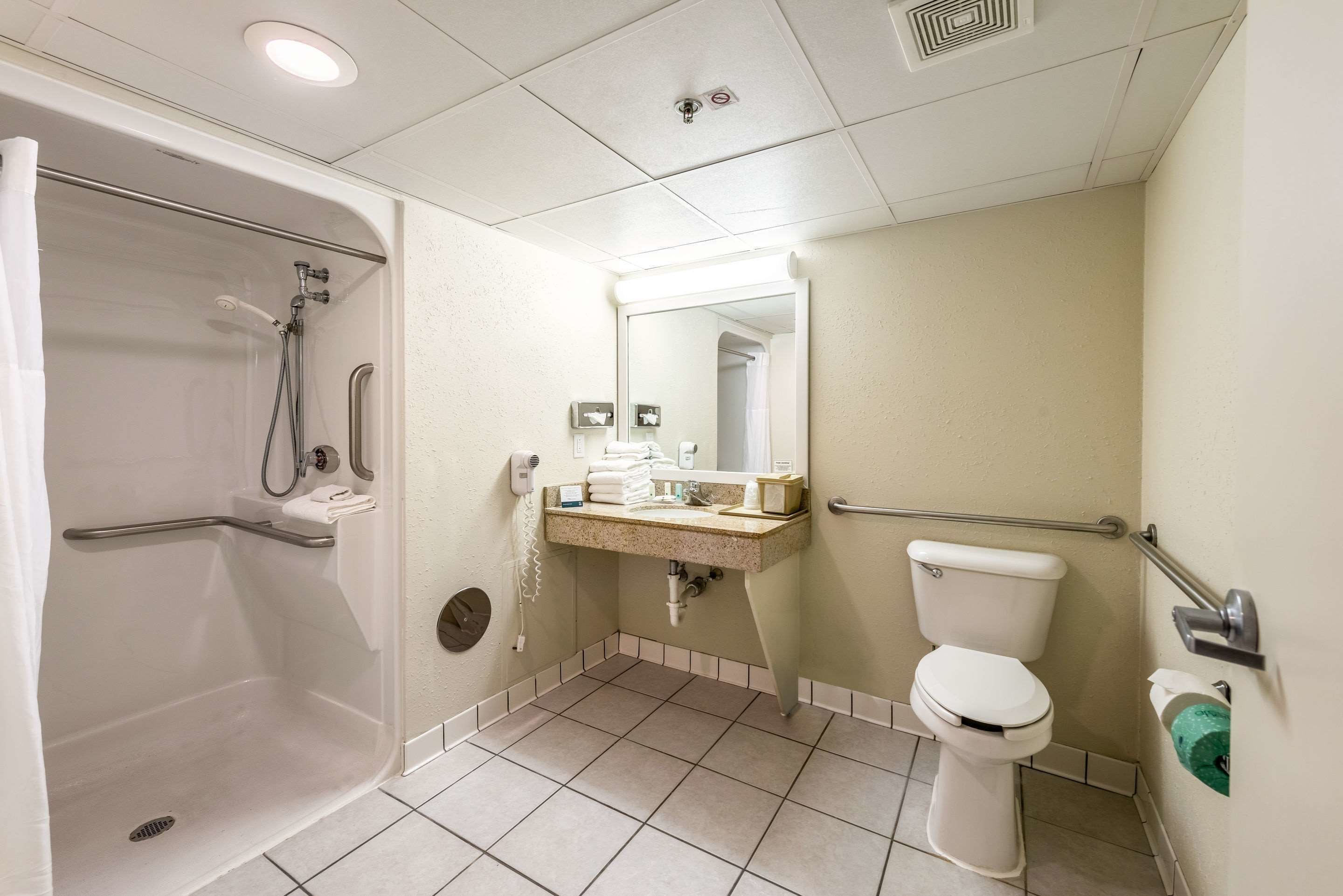 A bathroom with a shower, toilet, sink, and hand dryer.