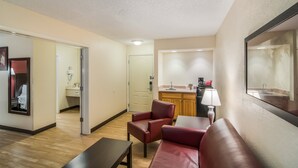 Habitación de hotel con piso de madera, un sofá de cuero rojo, una mesita y un espejo, además de una kitchenette al fondo.