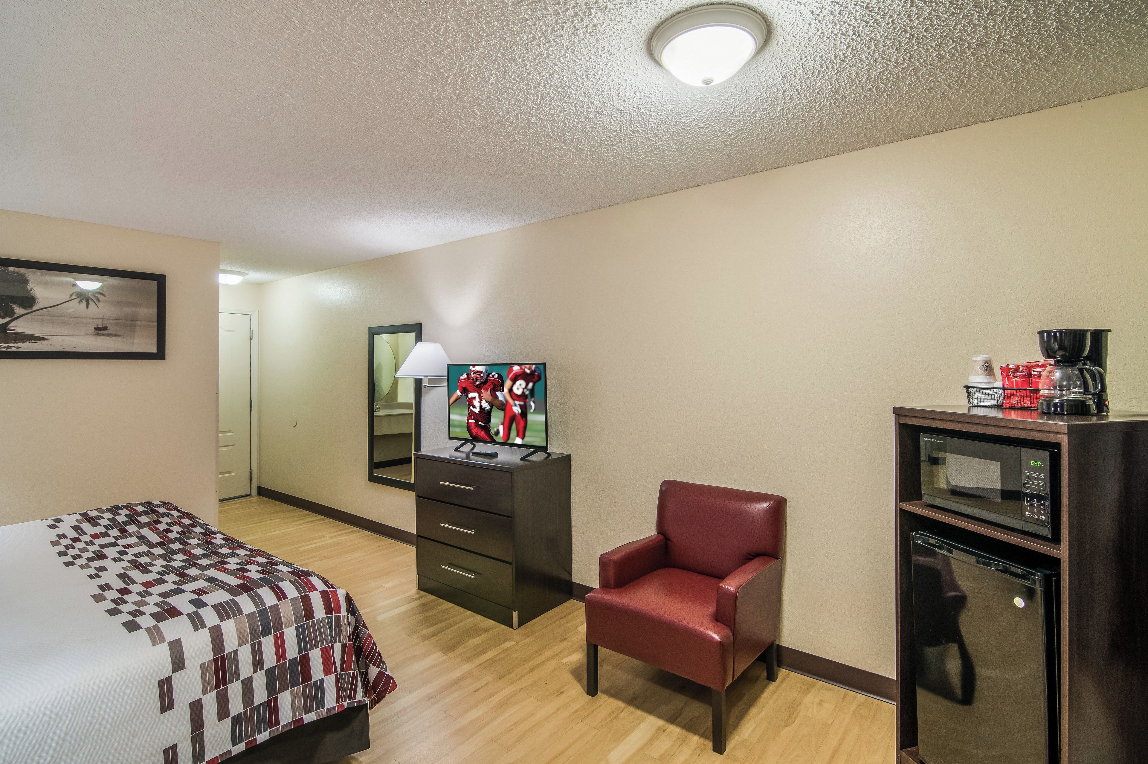 A hotel room with a bed, a TV, a chair, a desk with a coffee maker, and a microwave.