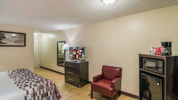 A hotel room with a bed, a TV, a chair, a desk with a coffee maker, and a microwave.