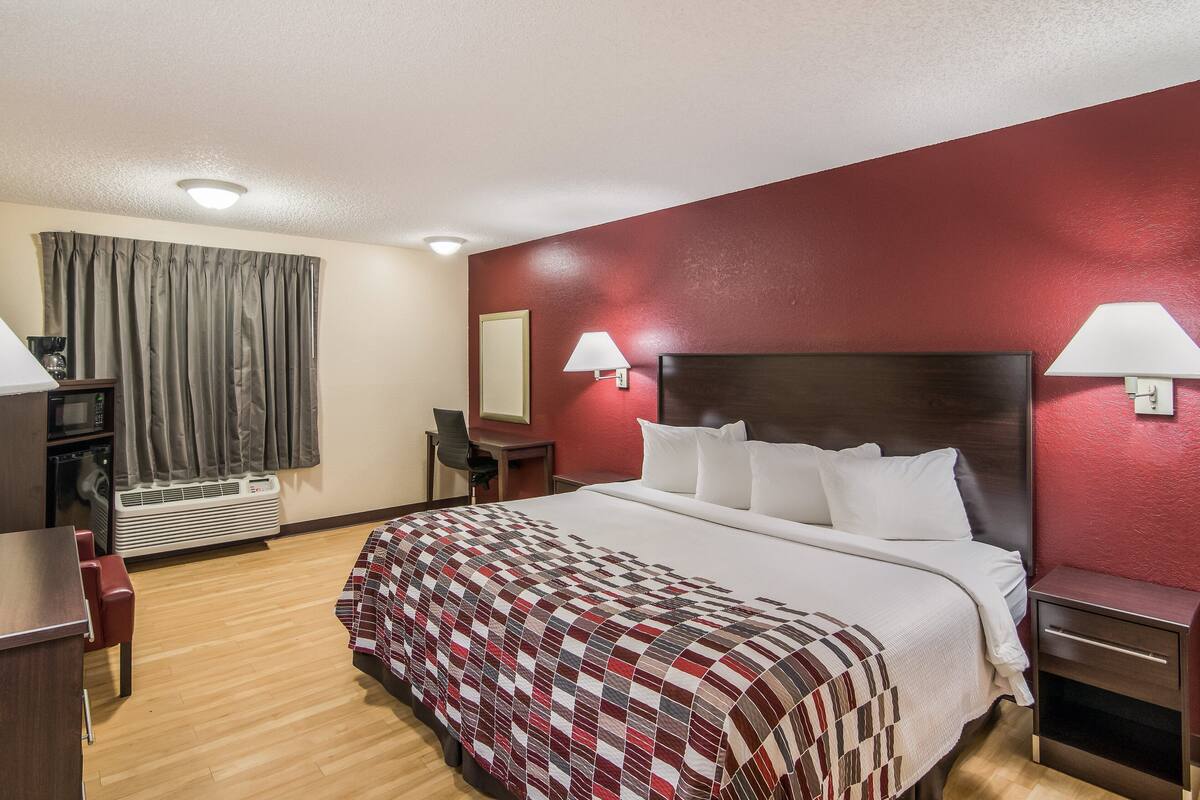 Una habitación de hotel con una cama grande, un escritorio, una silla, un televisor y una lámpara.