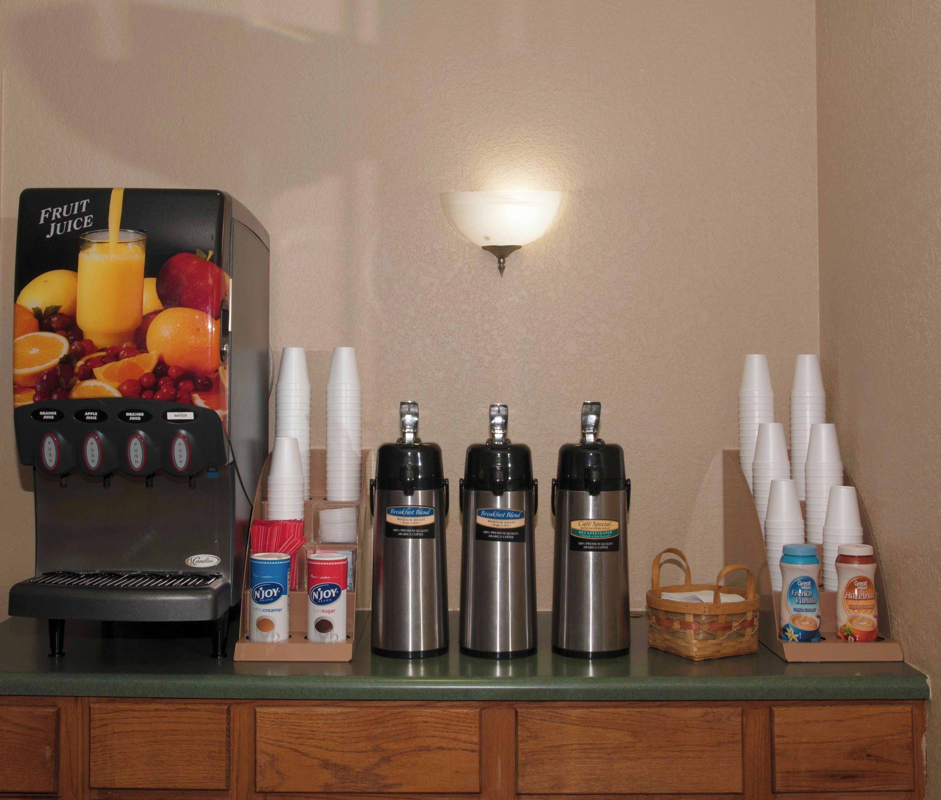 A beverage station with a fruit juice dispenser, coffee makers, and creamer dispensers.