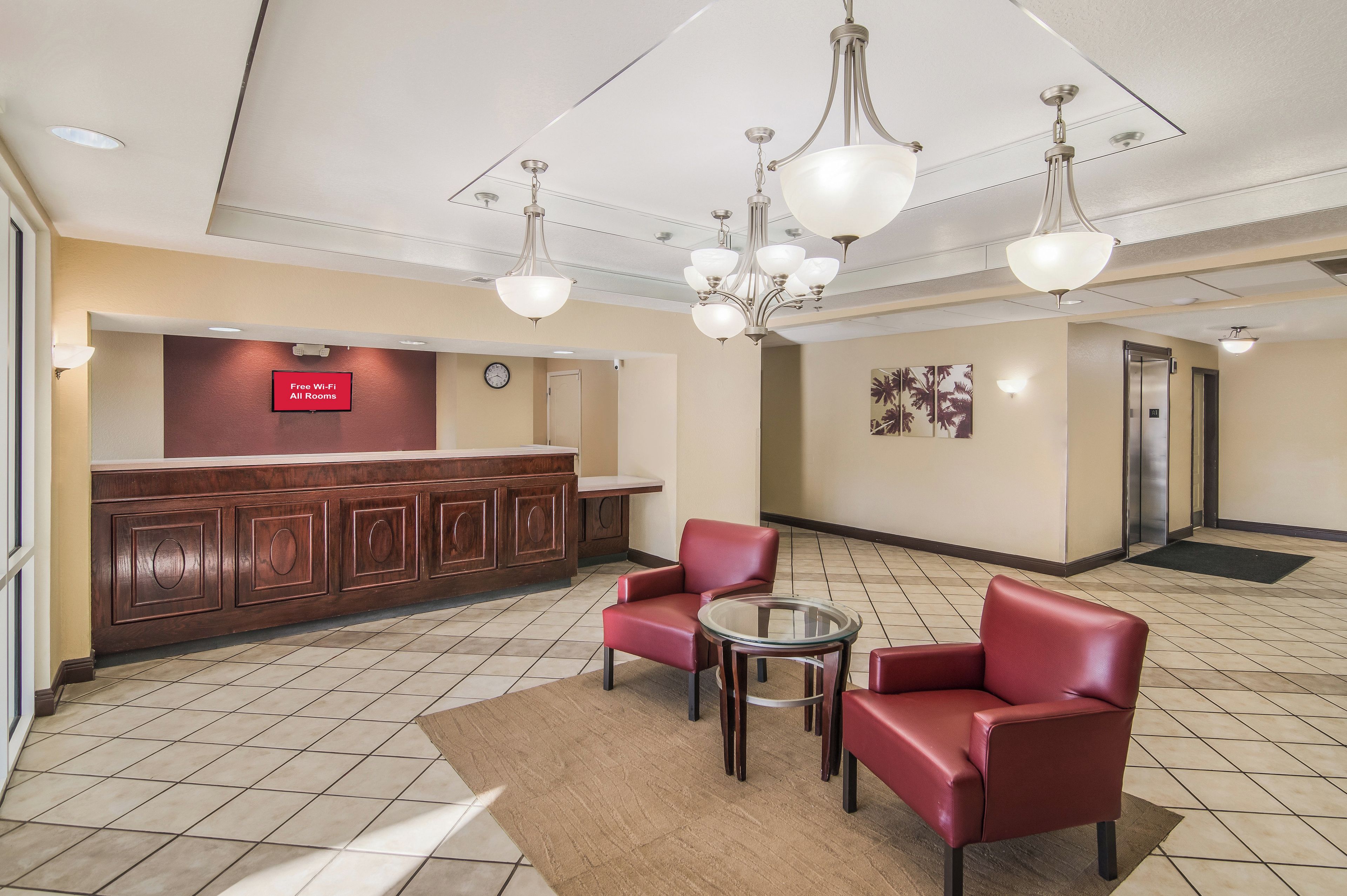 Un hall d’hôtel comprenant un comptoir d’accueil, une horloge, une œuvre d’art accrochée au mur et un espace détente avec deux fauteuils et une petite table.