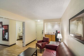 Une chambre d’hôtel équipée d’un canapé, d’une table, d’une kitchenette et d’une salle de bain, le tout visible à travers une porte ouverte.