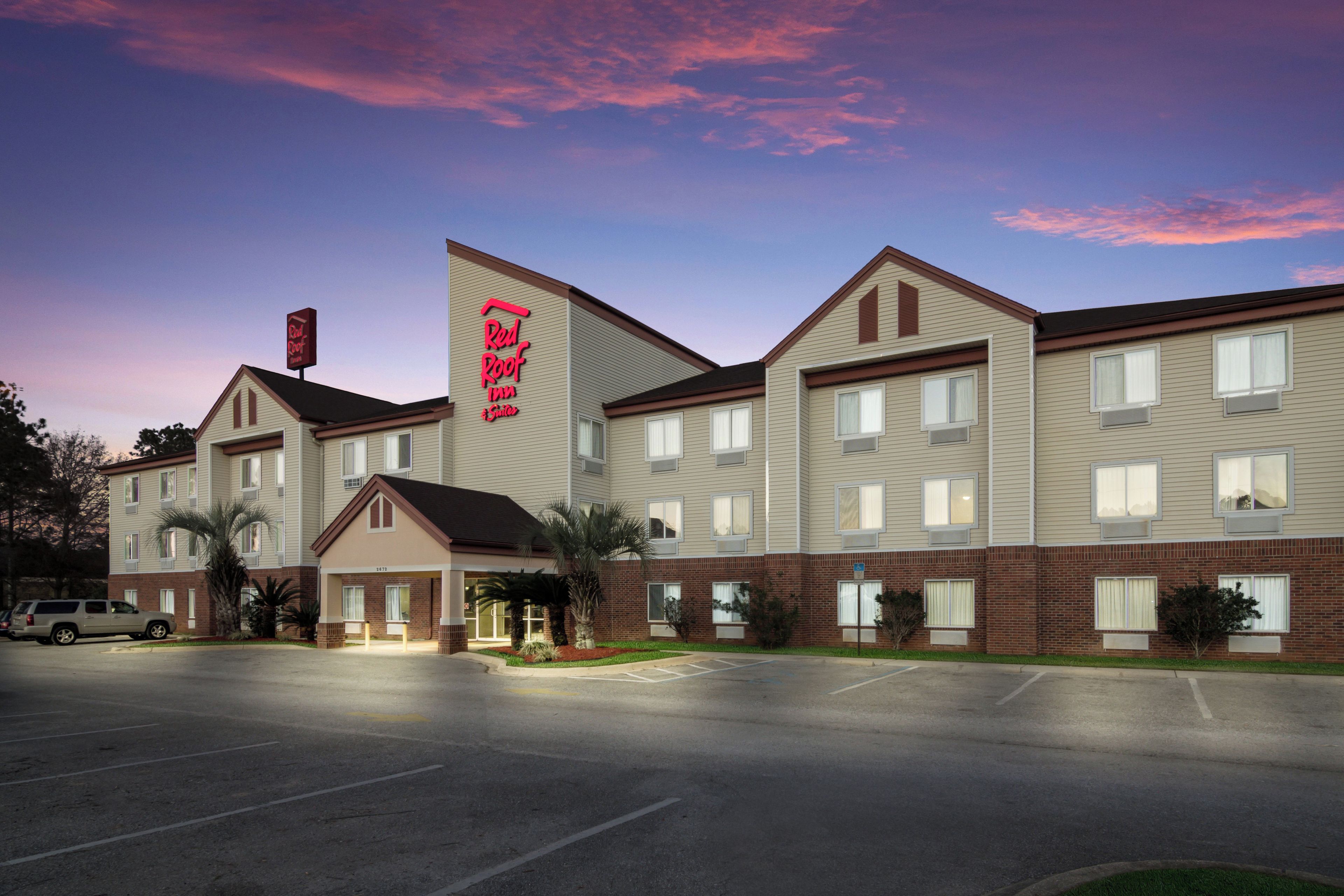A hotel with a prominent red sign, multiple windows, and a parking lot.