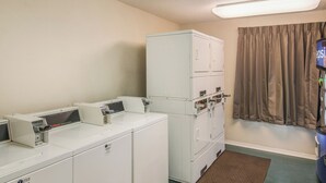 A laundry room with stacked washers and dryers, a commercial washer, and a window with curtains. - Red Roof Inn & Suites Pensacola East - Milton (Milton)