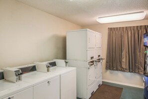 A laundry room with stacked washers and dryers, a commercial washer, and a window with curtains. - Red Roof Inn & Suites Pensacola East - Milton (Milton)