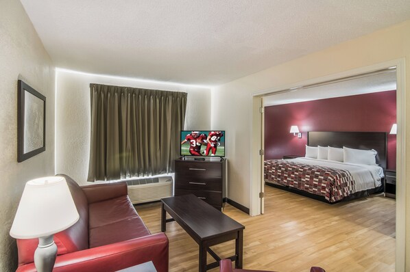 Habitación de hotel con televisión, sofá, escritorio, cama y baño visible a través de una puerta abierta.