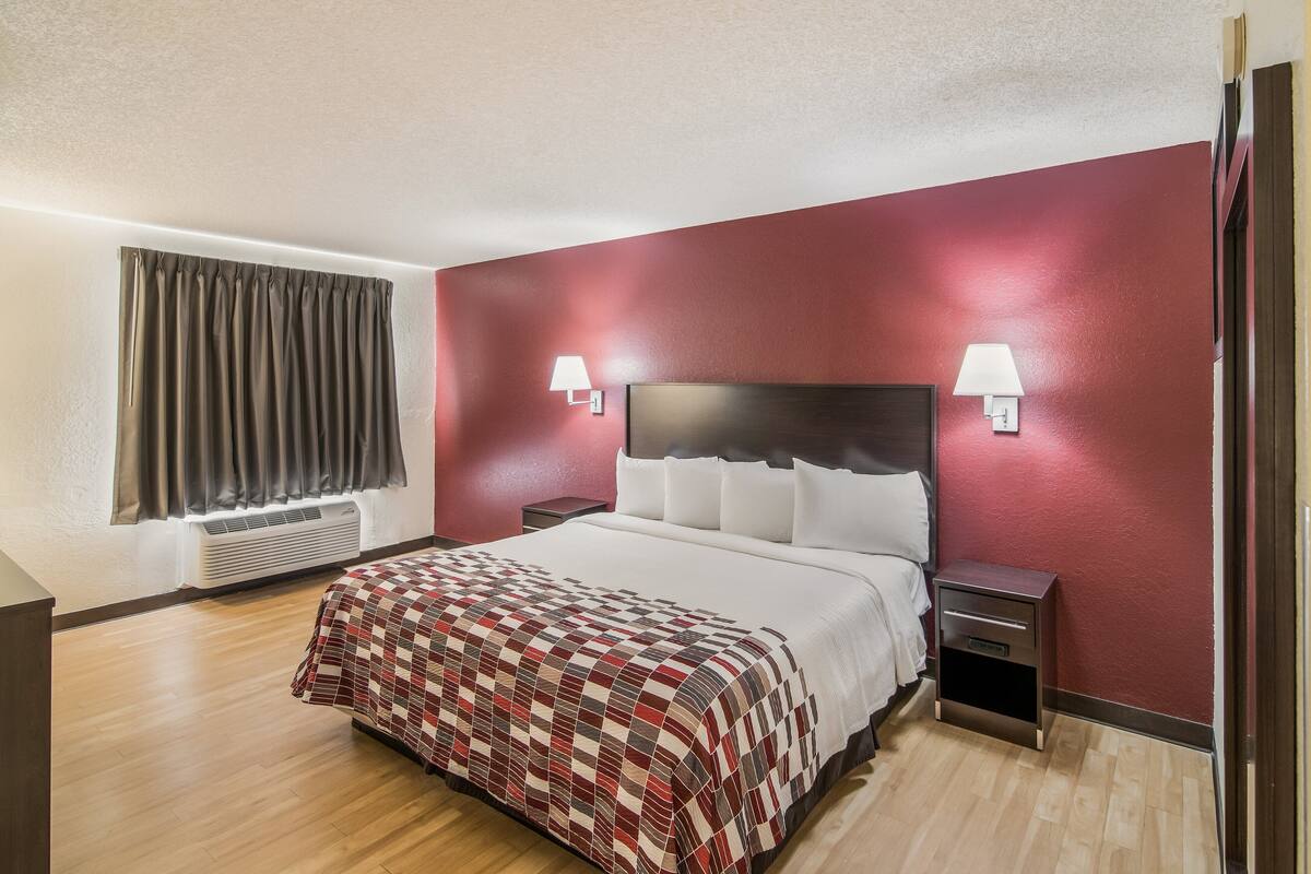Habitación de hotel con cama, dos mesitas de noche, una ventana con cortinas y una lámpara de pared.