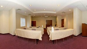 Un salón de conferencias con varias mesas y sillas, una pizarra y una puerta al fondo.