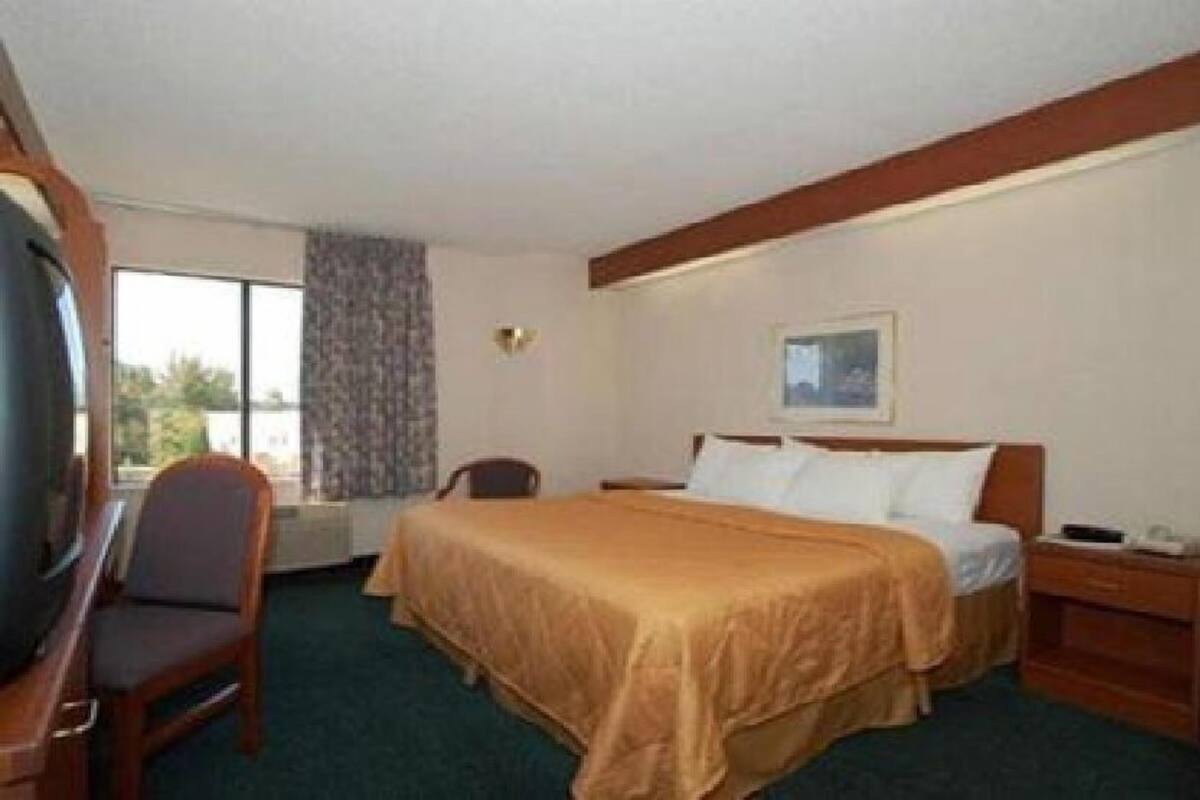 A hotel room with a bed, a chair, a desk, a television, and a window.