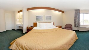 Una habitación de hotel con una cama grande, una mesita de noche con lámpara, una silla, una ventana con cortinas y un teléfono montado en la pared.