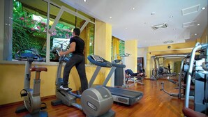 Un gimnasio con cintas de correr, elípticas y máquinas de pesas, amplias ventanas que dan a zonas verdes, y suelo de madera.