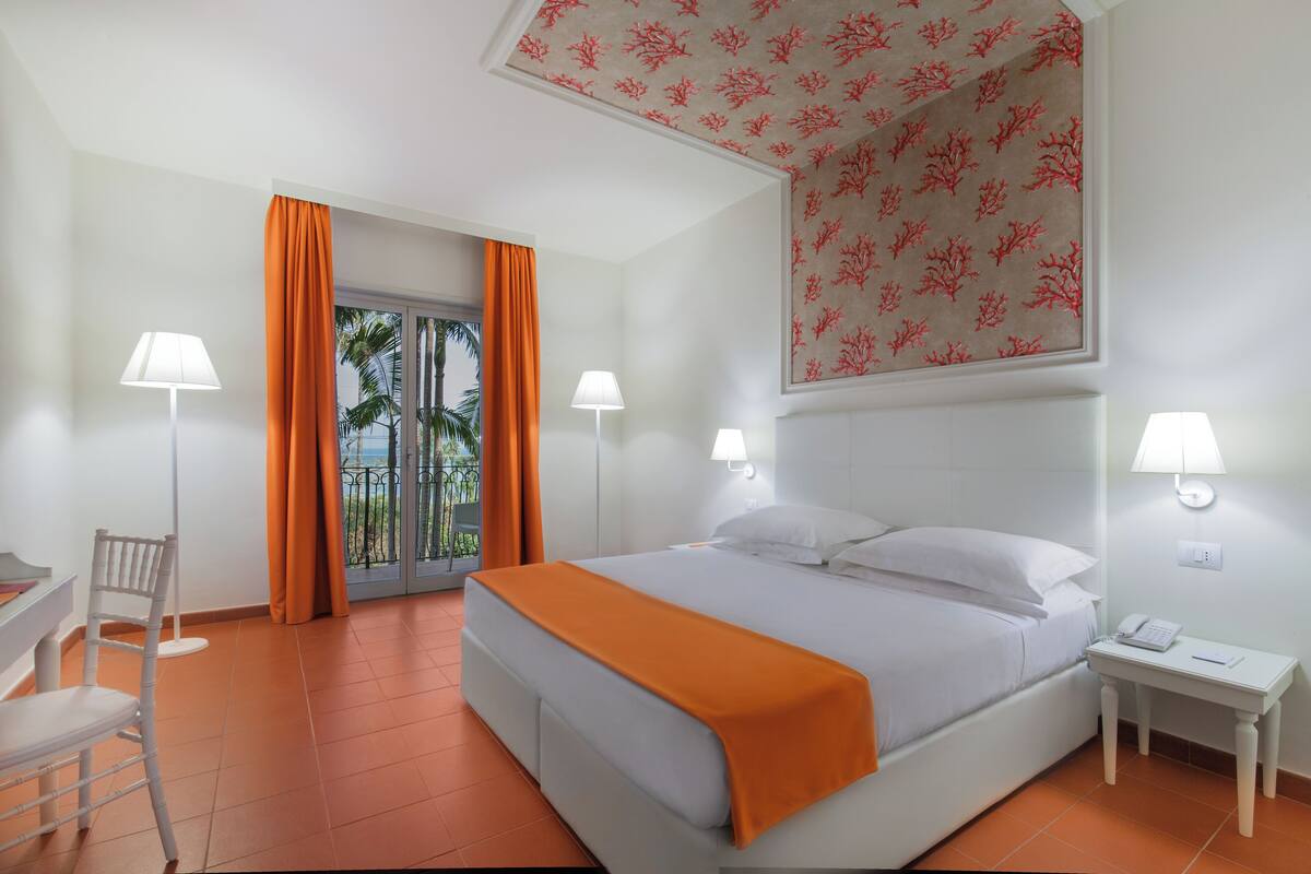 Une chambre d’hôtel avec un lit, deux lampes de chevet, un bureau avec une chaise et une fenêtre avec des rideaux.