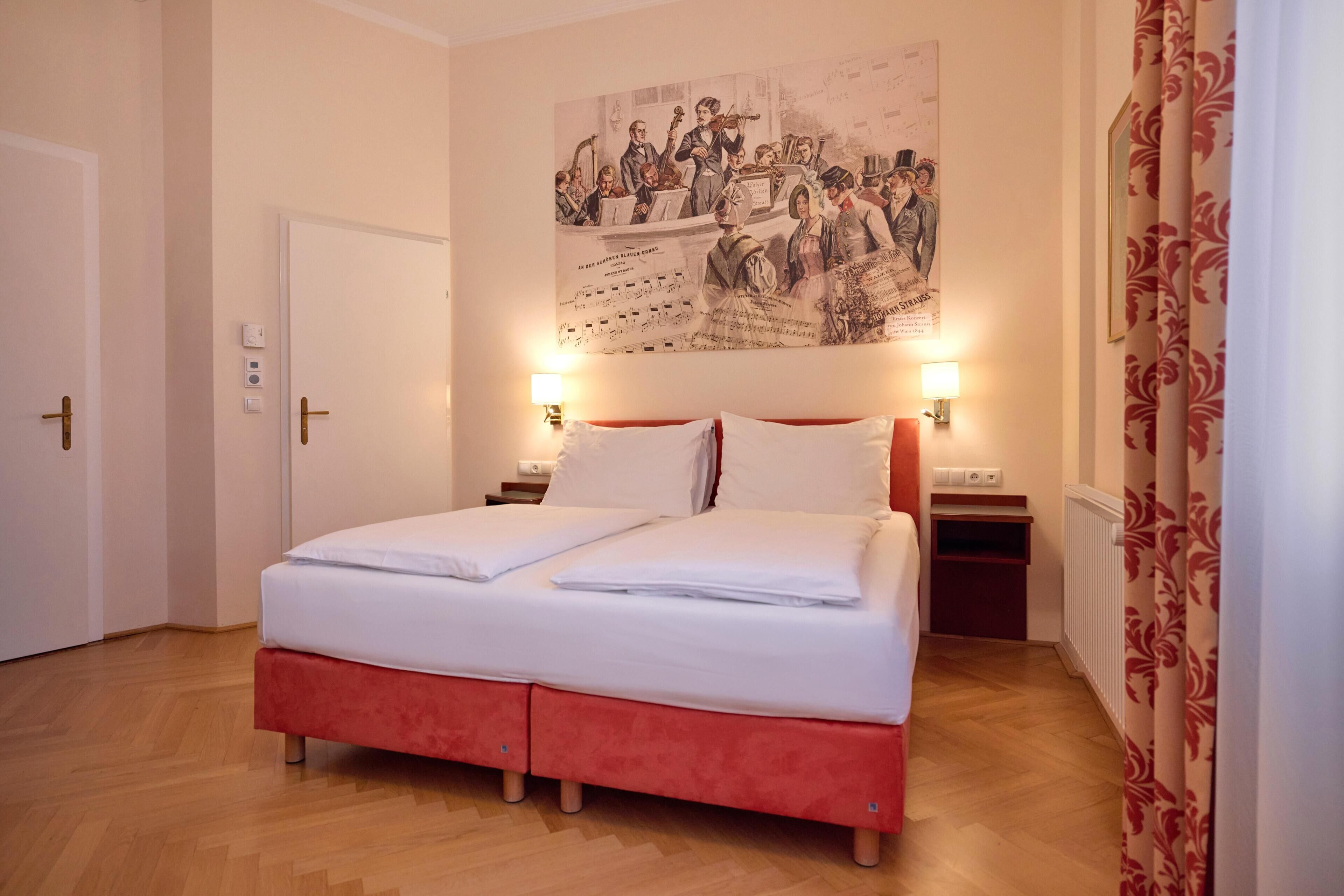 A double bed with white linens, a red headboard, two bedside tables with lamps, a wall-mounted poster, and a wooden floor.