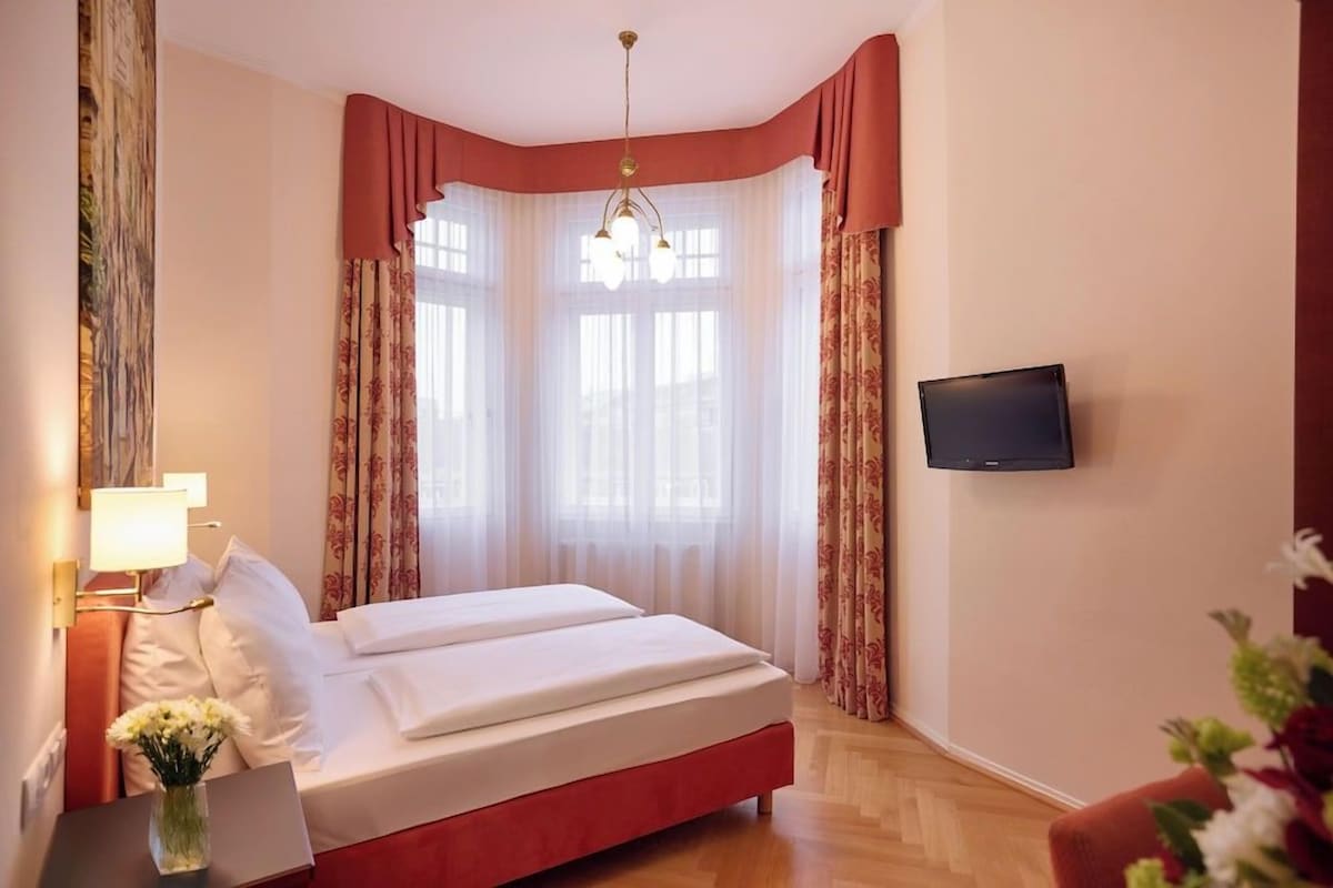 A hotel room with a bed, a TV mounted on the wall, and a window with curtains.