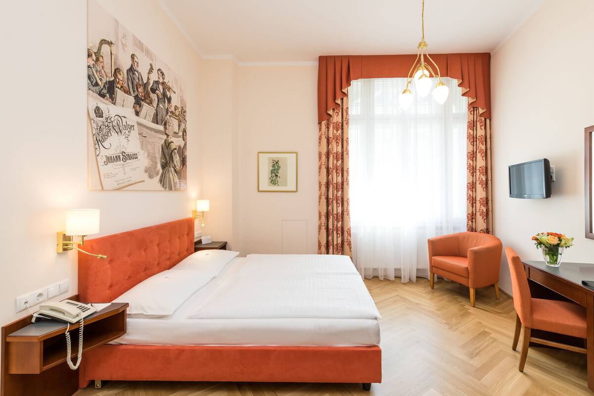 A hotel room with a bed, a desk, a chair, a telephone, a television, and a poster on the wall.