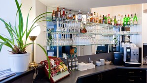 Uma área de bar com prateleiras cheias de garrafas de bebidas, copos e uma máquina de café.