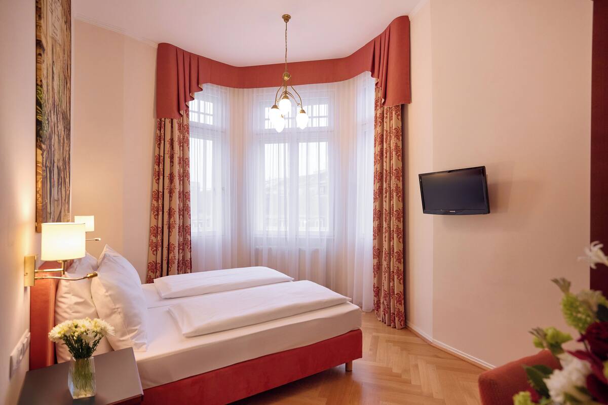 A hotel room with a bed, a TV mounted on the wall, and a window with curtains.