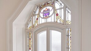 Una ventana de esquina con vidrieras de colores, molduras blancas y barandilla de madera.
