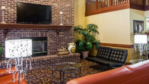 A living room with a brick fireplace, a flat-screen TV, leather sofas, a glass coffee table, and a staircase with wooden railings. - Quality Inn Bolingbrook I-55 (Bolingbrook)