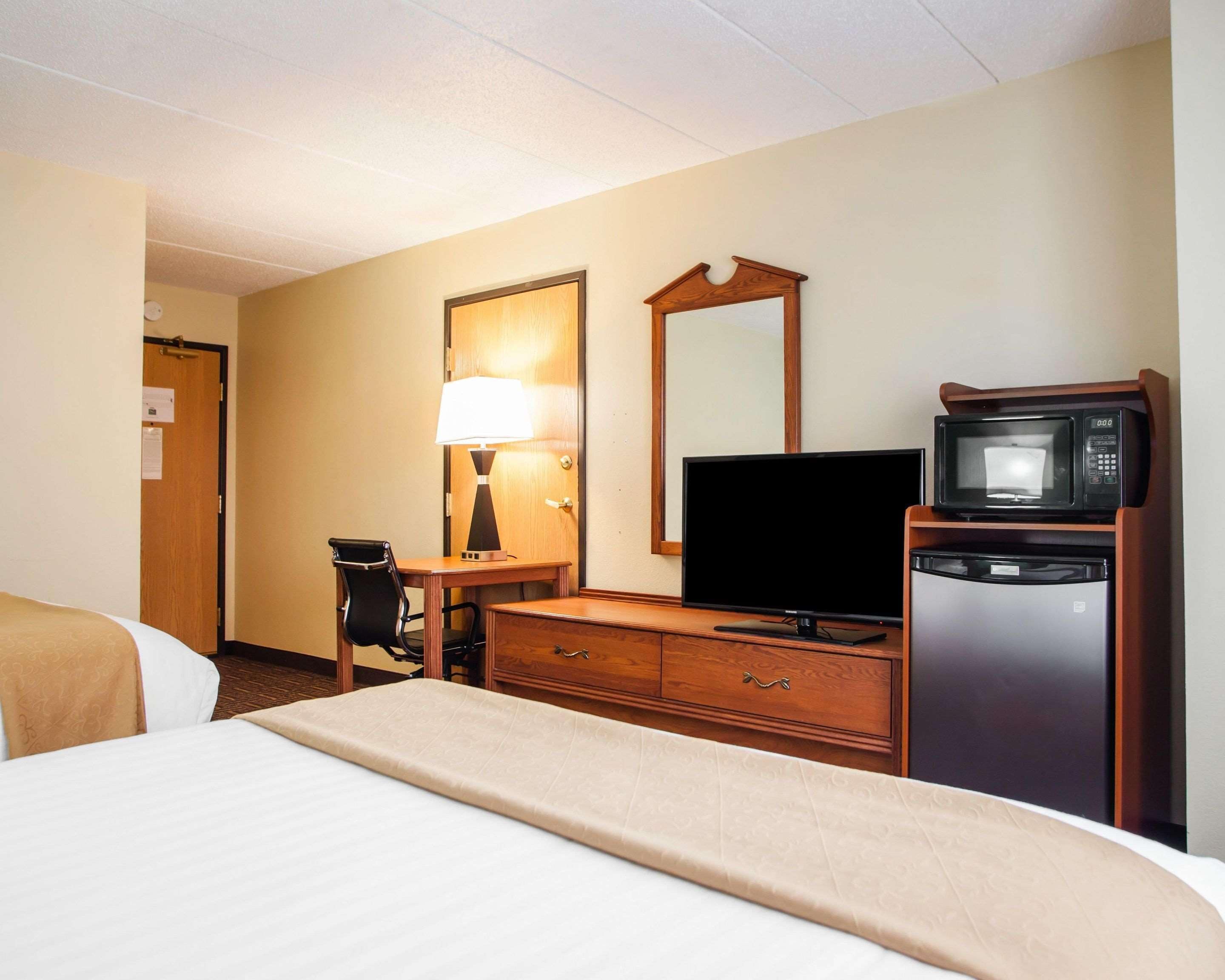 A hotel room with a bed, a desk with a lamp, a television, a microwave, and a refrigerator.