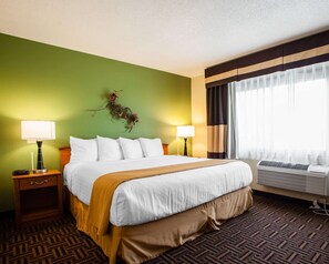 A hotel room with a bed, two bedside lamps, a wall-mounted air conditioner, and a window with curtains.