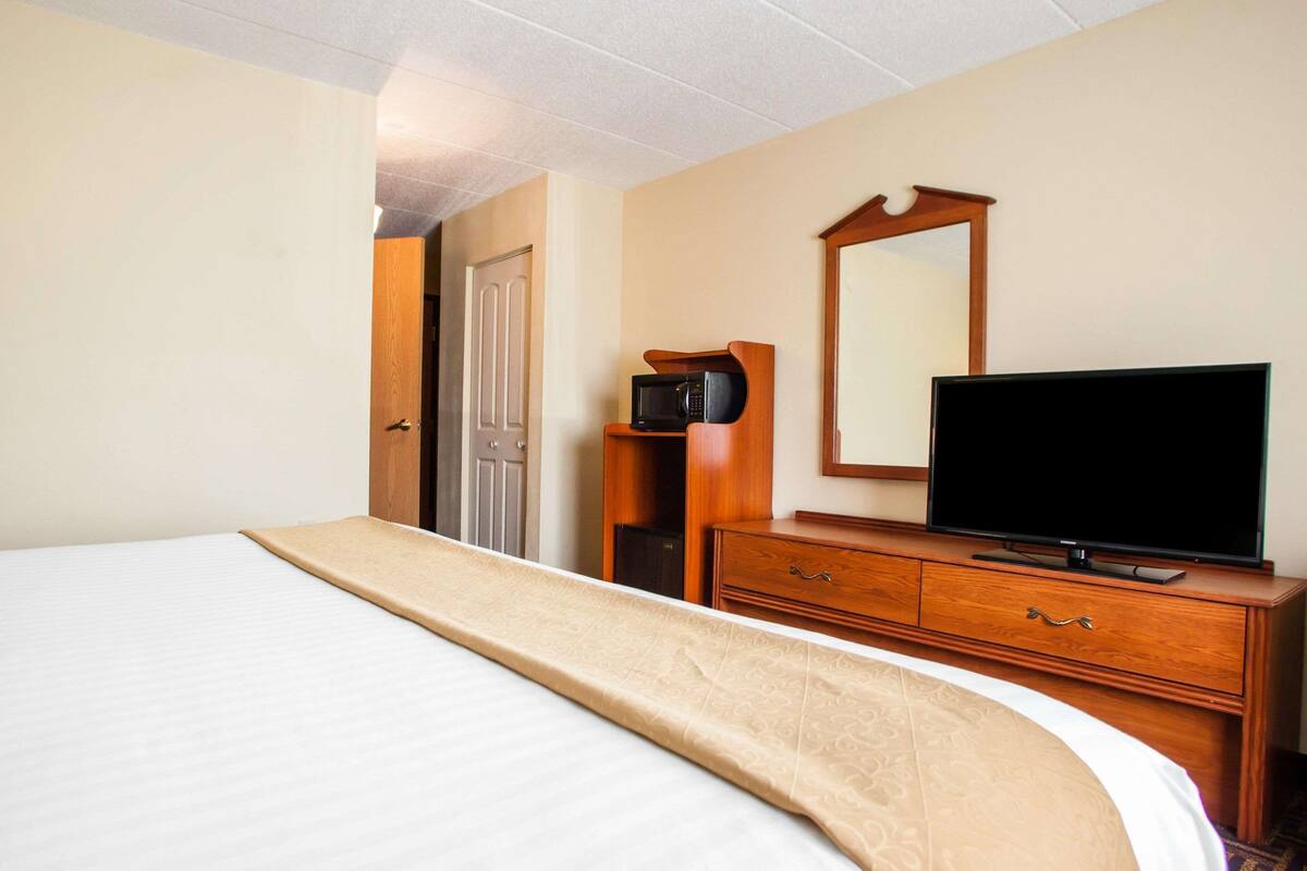 A hotel room with a large bed, a wooden dresser with a flat-screen TV, a microwave, and a mirror on the wall.