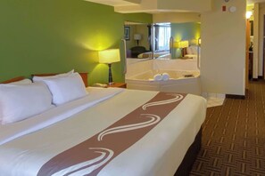 A hotel room with a large bed, a bathroom with a bathtub, and a mirror reflecting the room.