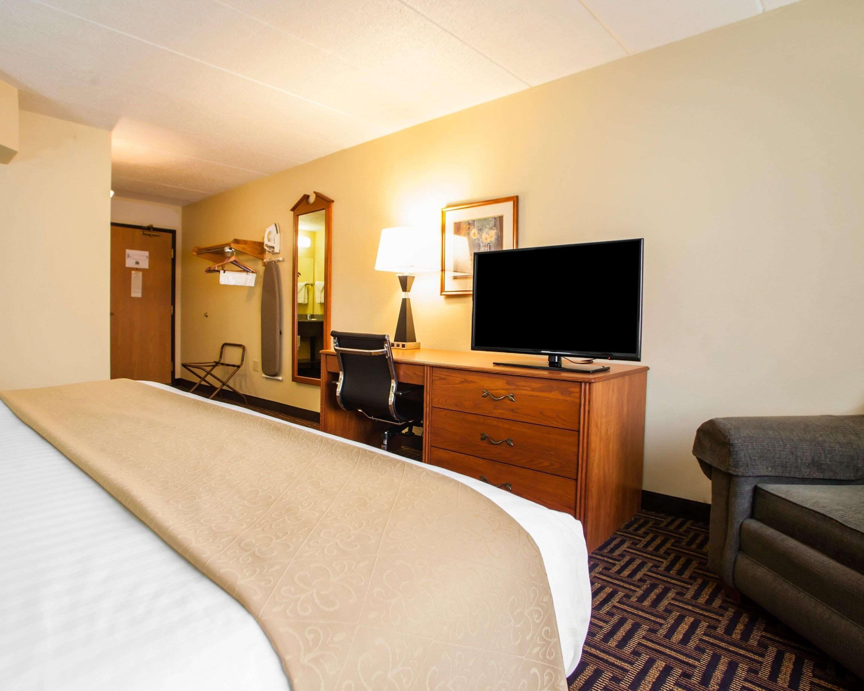 A hotel room with a bed, a desk with a television, a chair, a lamp, and a mirror.