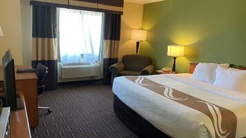 A hotel room with a bed, desk, chair, air conditioning unit, and two lamps.
