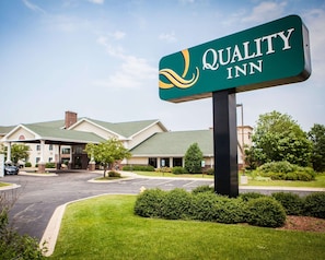 A Quality Inn hotel with a green sign, a parking lot, and a well-maintained lawn.