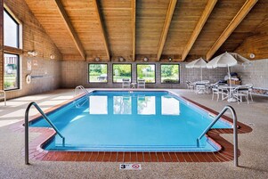 Una piscina interior con techo de madera, ventanas amplias y una zona de estar con sombrillas.