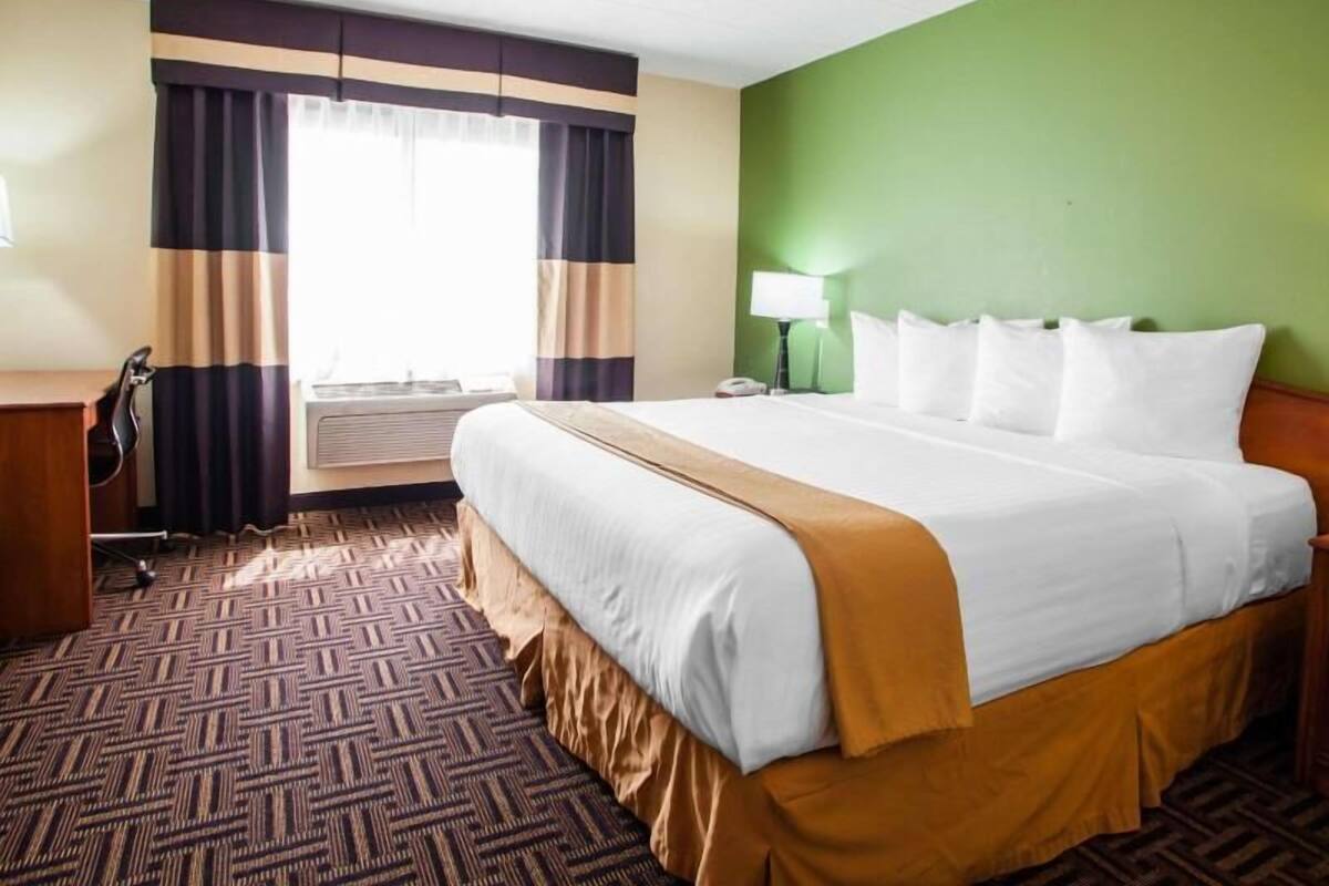 A hotel room with a large bed, a desk, a chair, a lamp, and a window with curtains.