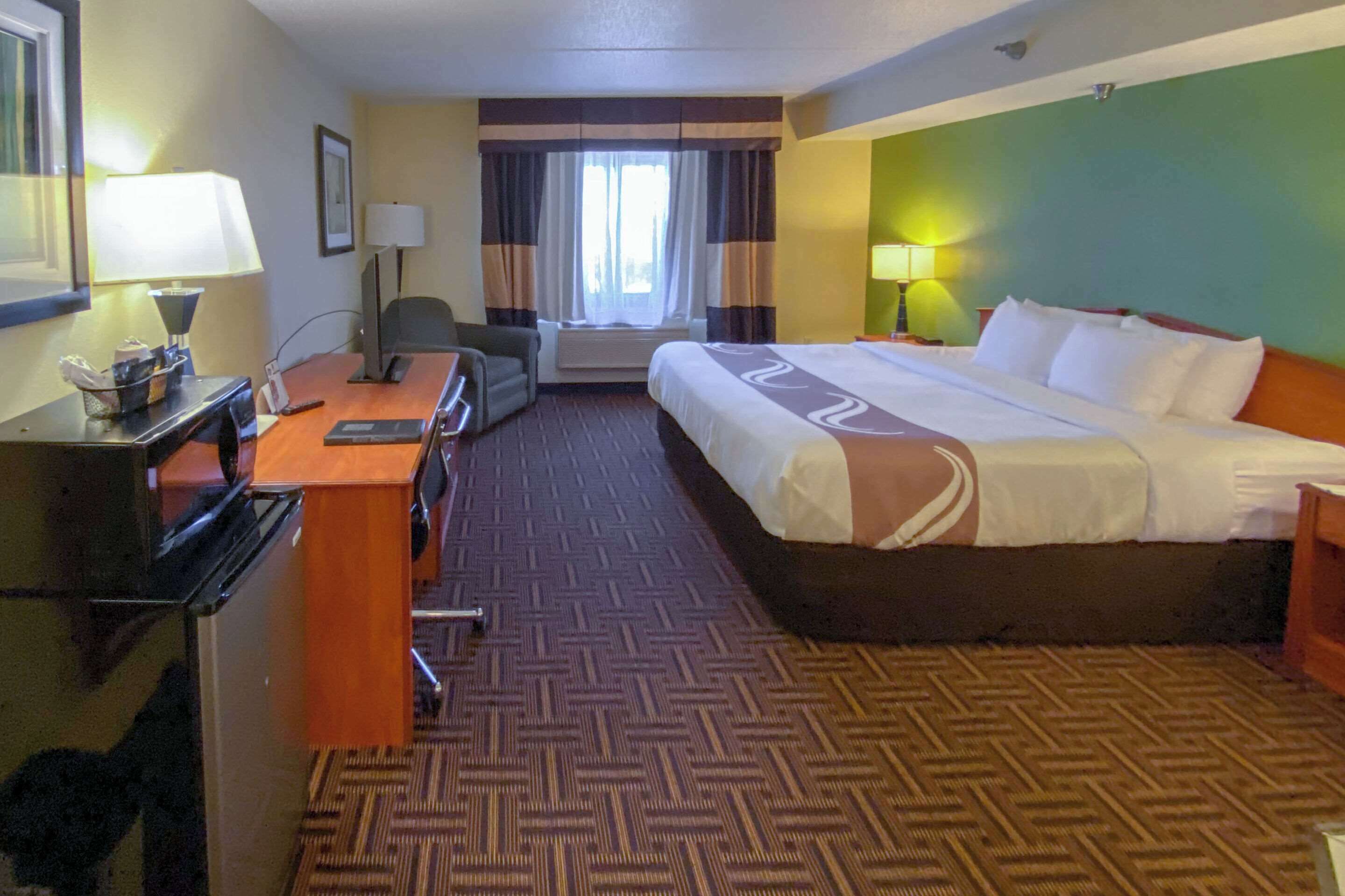 A hotel room with a bed, desk, chair, and a window with curtains.