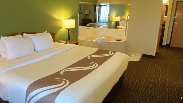 A hotel room with a large bed, a bathroom with a bathtub, and a mirror. - Quality Inn Bolingbrook I-55 (Bolingbrook)