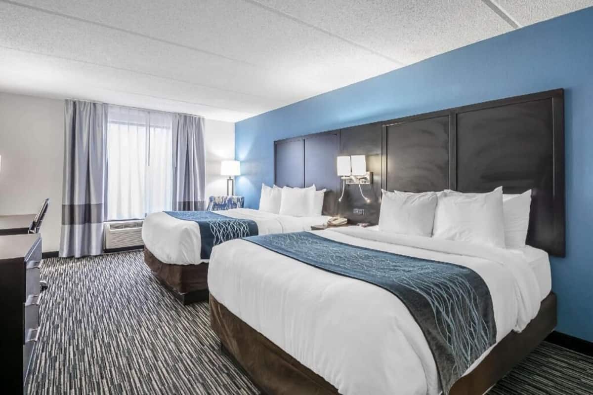 A hotel room with two beds, a desk, a chair, and a large window with curtains.