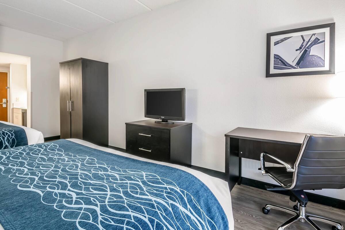 A hotel room with a bed, a desk, a chair, a TV, and a wardrobe.