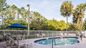 A swimming pool with lounge chairs and a blue umbrella, surrounded by a fence and palm trees.