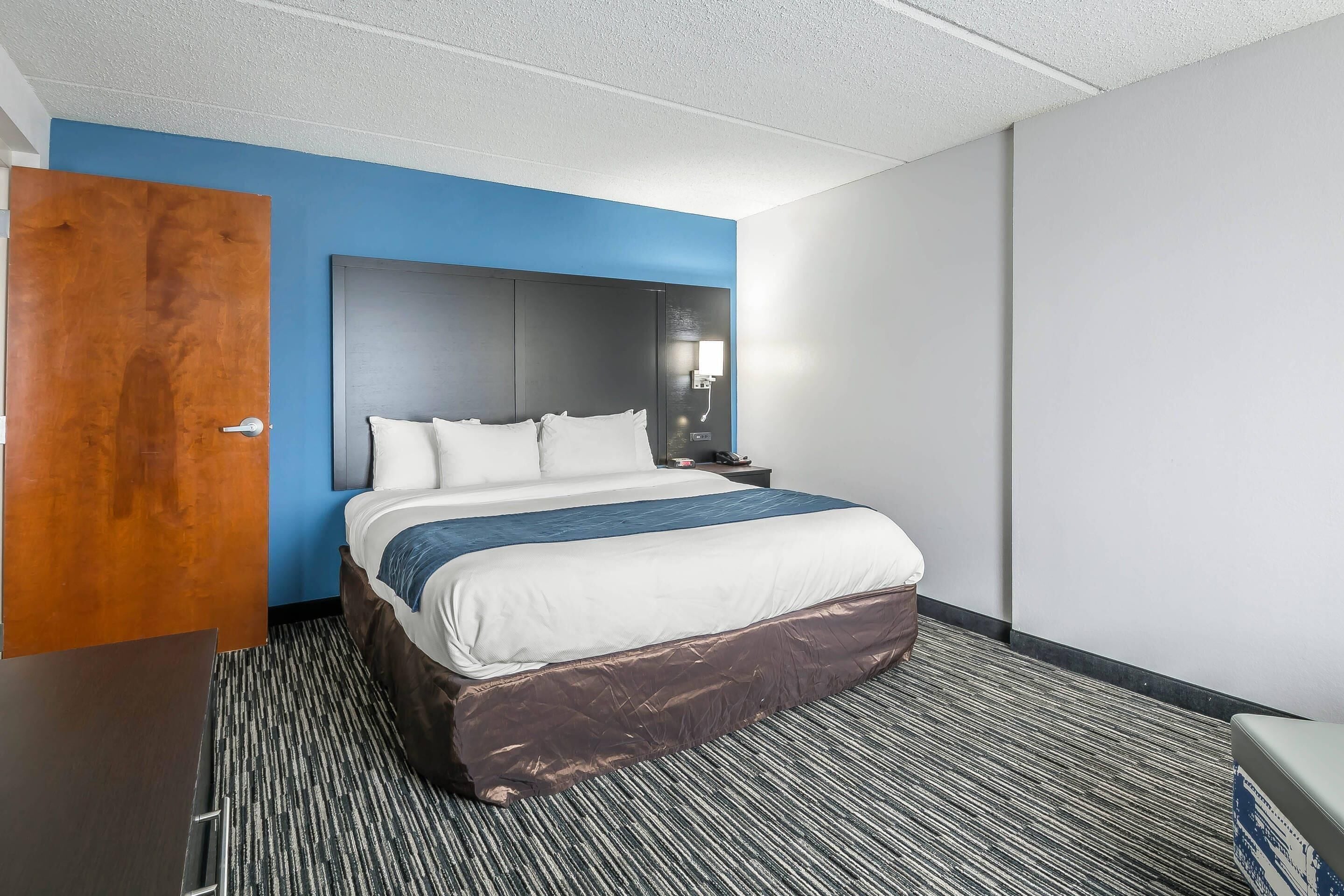 Una habitación de hotel con una cama, una mesita de noche, una lámpara de pared y una puerta.