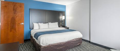 Una habitación de hotel con una cama, una mesita de noche, una lámpara de pared y una puerta.