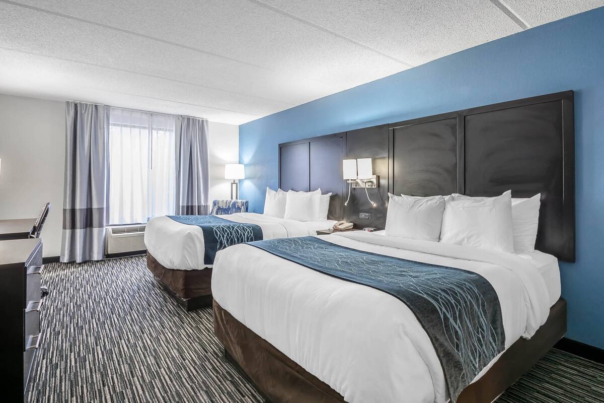 A hotel room with two beds, a desk, and a large window with curtains.