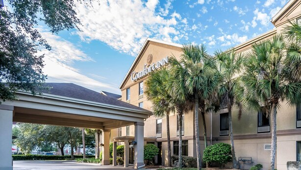 A Comfort Inn hotel with a covered entrance, palm trees, and a clear sky.