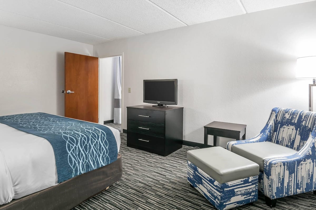 A hotel room with a bed, a dresser, a television, and a patterned armchair.