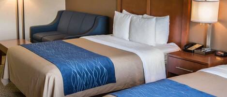 Habitación de hotel con dos camas, un escritorio, una silla, una lámpara y cuadros en la pared.