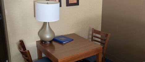A hotel room with a wooden table, two chairs, a lamp, and a bed.