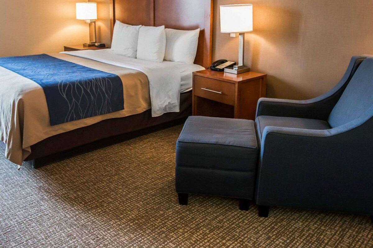 A hotel room with a bed, bedside tables, a chair, and a carpeted floor.