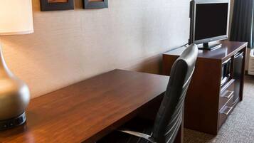 Habitación de hotel con un escritorio de madera, una silla de cuero negro, un televisor sobre un mueble y dos cuadros en la pared.