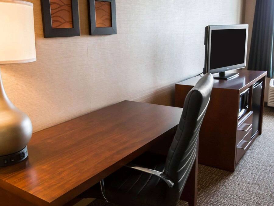 Habitación de hotel con un escritorio de madera, una silla de cuero negro, un televisor sobre un mueble y dos cuadros en la pared.