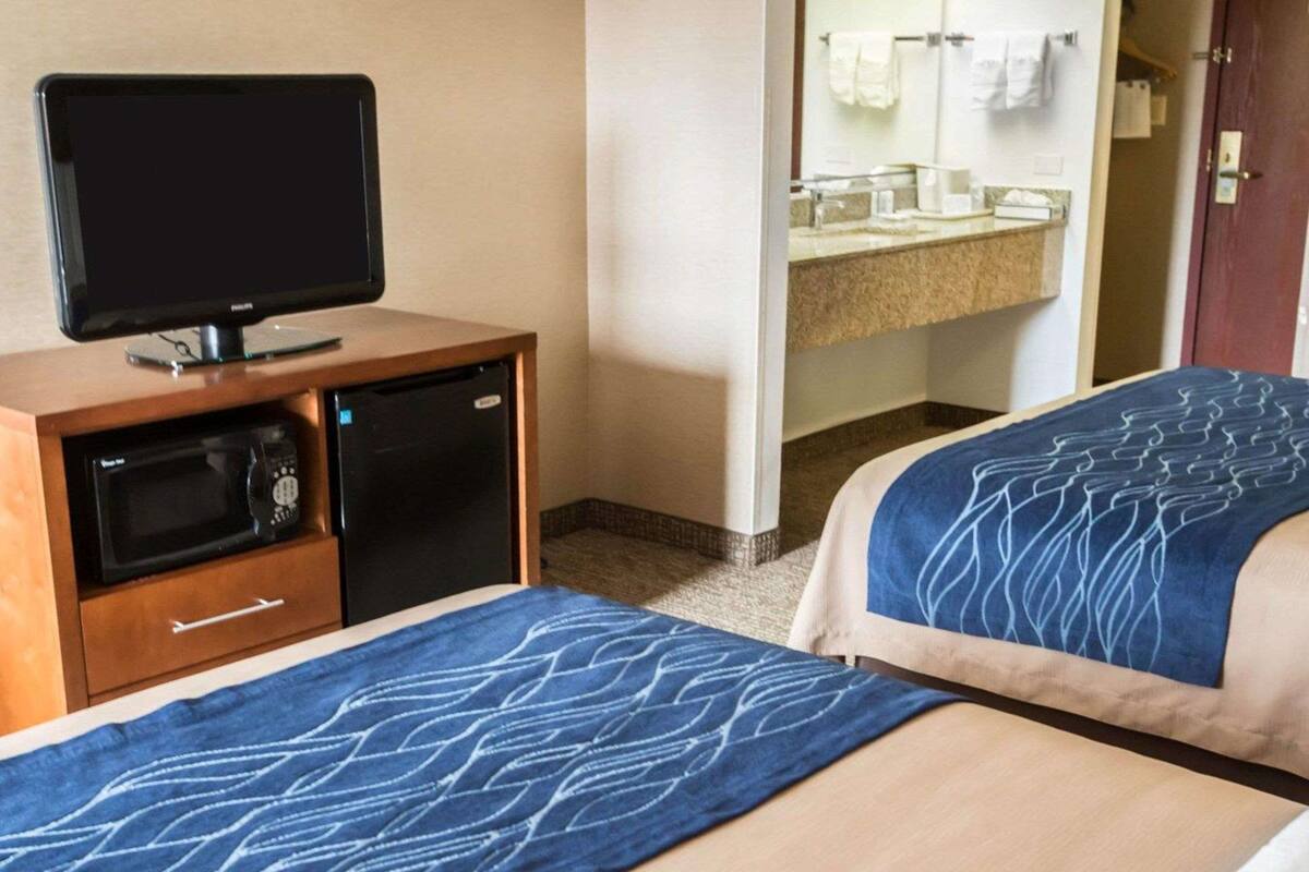 A hotel room with two beds, a TV, a microwave, and a bathroom visible through an open door.